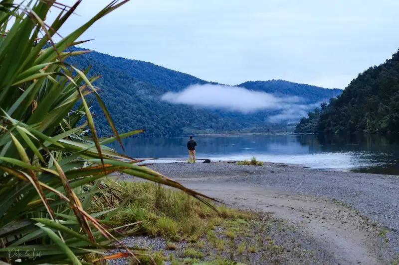 Un nomade en voyage avec son café sur le bord de l'eau devant les montagnes et les nuages